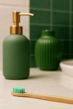 Load image into Gallery viewer, Green soap dispenser, bamboo toothbrush, and green vase on a bathroom counter.