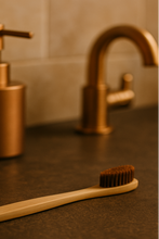 Load image into Gallery viewer, Bamboo toothbrush on a brown countertop with bronze faucet and soap dispenser in the background.