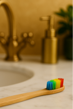 Load image into Gallery viewer, Bamboo toothbrush with rainbow bristles on a bathroom counter.