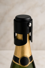 Load image into Gallery viewer, A black and rose gold champagne cork stopper fitted on a champagne bottle with a visible brand label.