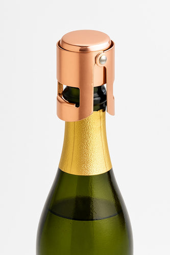 A rose gold champagne cork stopper fitted on a champagne bottle.