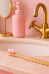 Bamboo toothbrush on a pink sink with a gold faucet and mirror in the background.